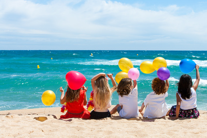 Children sitting on beach with color balloons.
